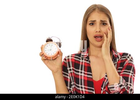 Young woman looking terrified screaming with her hand to her face holding alarm clock isolated on white copy space. Time management, timing, being lat Stock Photo