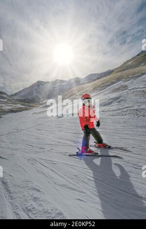 child with helmet and red jacket learns to ski with the sun at the background, in the ski resort of Boi Taull, Pyrenees Lleida, Spain, vertical Stock Photo
