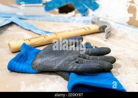 A pair of dirty gloves and a hammer lie on a counter with a sheetrock repair behind. Stock Photo