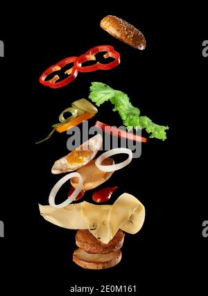 big tasty burger with meat cutlet, cheese, fried egg, tomatoes, cucumber pieces and green lettuce, fast food levitates, black background Stock Photo