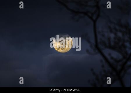 Full Moon in December 2020 rising above mountain at dusk on a cloudy evening Stock Photo