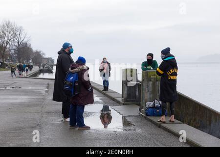 Seattle, Washington, USA. 1st January, 2021. Members of the Notorious Alki Swimmers open-water swimming group talk after taking the plunge at the annual West Seattle Polar Bear Swim at Alki Beach Park. Organizers arranged physically distanced sites and staggered timing along Alki Beach for participants amid a recent moderation of COVID-19 cases in the city. Credit: Paul Christian Gordon/Alamy Live News Stock Photo