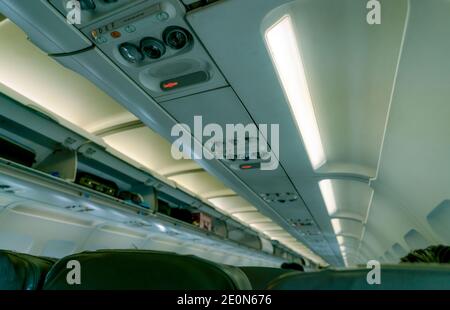 Selective focus on overhead reading light in commercial airplane on blurred overhead bin with opened door show carry on in overhead stowage. Airplane Stock Photo