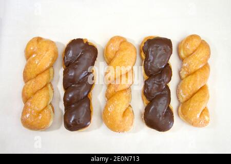Top view flat lay of row of alternating glazed twist donut and chocolate covered glazed twist on parchment paper. Stock Photo