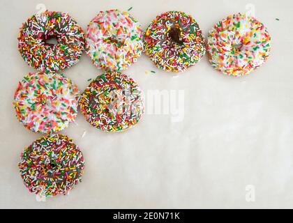 Flat lay view of many frosted donuts, chocolate and vanilla with candy sprinkles arranged in a row top and side on a parchment paper Stock Photo