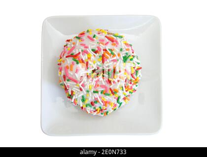 Top view flat lay of one vanilla cake donut with vanilla frosting covered in bright colorful candy sprinkles on a small square off white porcelain pla Stock Photo