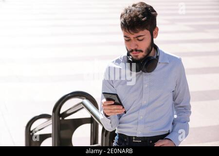 Young business man wearing headphones and using his smartphone. Businessman in a urban street of a city. Stock Photo