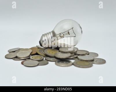 Isolated Bulb with coins. Money spent with light bulbs. Concept of energy efficiency Stock Photo
