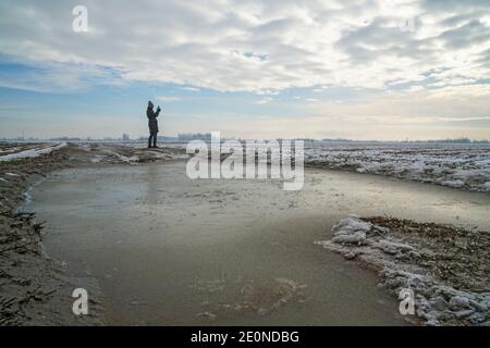 Mortara -12/29/2020: woman taking pictures with smarphone in a rice field landscape in winter in north italy Stock Photo