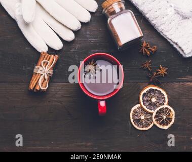 knitted mittens and red cup with a drink on a brown wooden table, top view.