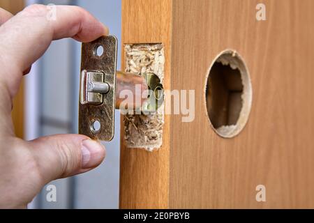 Carpenter shoves latch assembly of door knob through the edge bore. Stock Photo