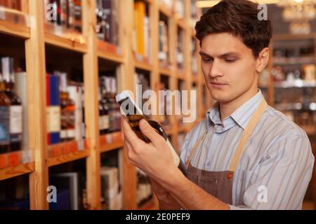 Handsome young male sommelier working at his store, reading label on a wine bottle, copy space Stock Photo