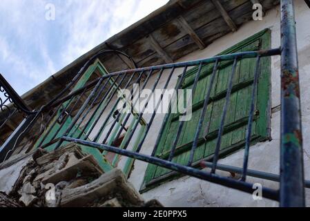 Green discoloured aged window next to a staircase with a  black rusty metal rail located in a small village Stock Photo