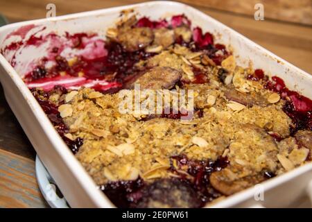 A baking trey of delicious plum and blackberry crumble on a wooden kitchen work top. Stock Photo