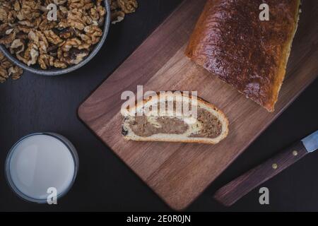 Homemade walnut roll on the wood cutting board. Fresh baked walnut roll with a glass of milk ready for breakfast. Hungarian traditional cake. Stock Photo