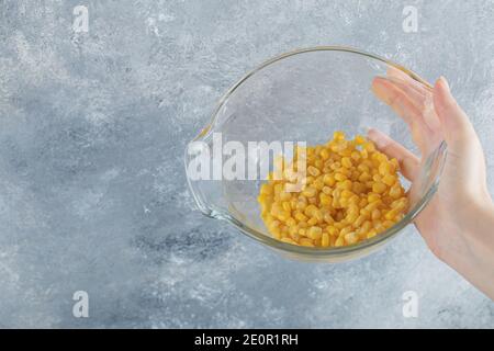 Female hand holding bowl of canned corns on marble background Stock Photo