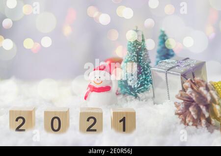 Happy New Year 2021 creative ideas at cubes on snow and background snowman and Christmas tree. Stock Photo