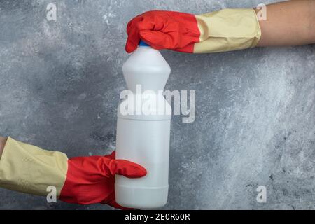 Hands in red gloves holding bleach on marble background Stock Photo
