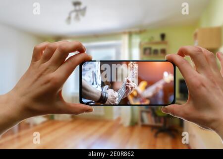 Online music lesson via mobile phone at home. Guitar teacher hands on screen. Stock Photo