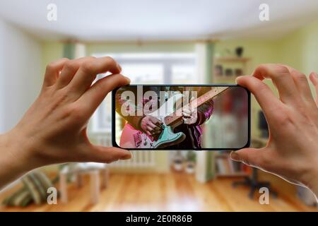 Online music lesson via mobile phone at home. Guitar teacher hands on screen. Stock Photo
