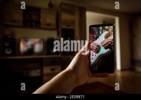 Online music lesson via mobile phone at home. Guitar teacher hands on screen. Stock Photo