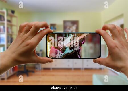 Online music lesson via mobile phone at home. Guitar teacher hands on screen. Stock Photo