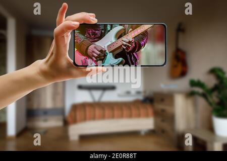 Online music lesson via mobile phone at home. Guitar teacher hands on screen. Stock Photo