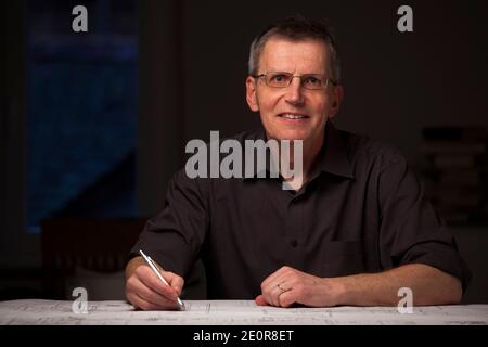 Smiling engineer or architect in dark shirt working at home by night - looking at camera Stock Photo