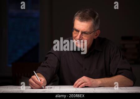 Concentrated engineer or architect in dark shirt working at home by night - focus on the face Stock Photo