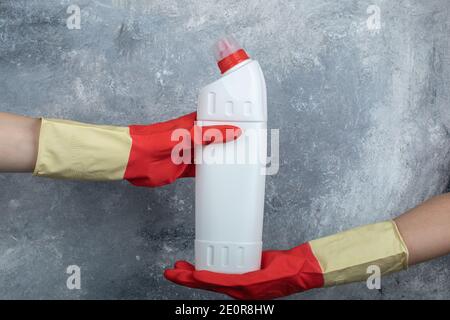 Hands in red gloves holding detergent on marble background Stock Photo
