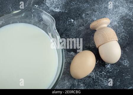 Glass bowl full of fresh milk and eggs on marble background Stock Photo