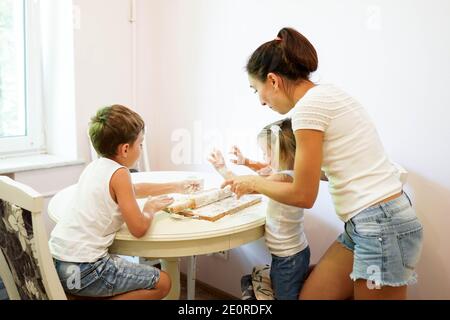 Portrait of a young mother with her little daughter and son sculpt a dough on a kitchen. Stock Photo