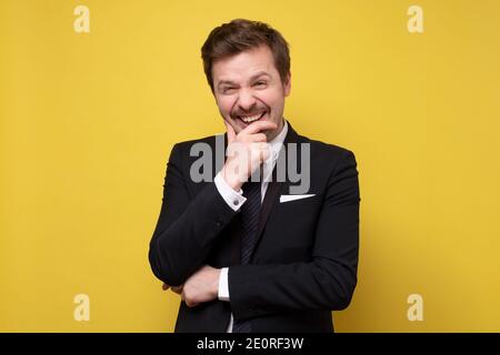 Young happy cheerful young man in suit laughing on your joke. Studio shot on yellow wall. Stock Photo