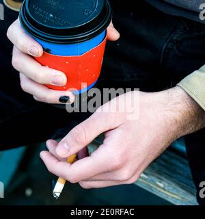 London UK, January 02 2021, Young Anonymous Man Holding A Cup Of Takeaway Caffe Nero Coffee An d A lit Cigarette Stock Photo