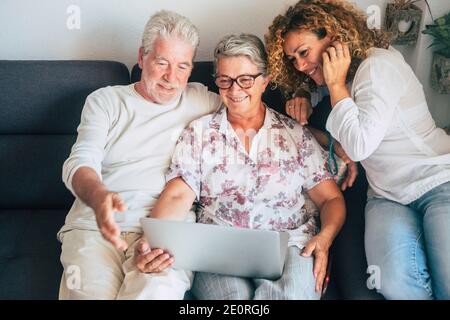 Cheerful happy old adult family at home use and enjoy laptop computer together - mixed and different generations from young woman to senior couple smi Stock Photo