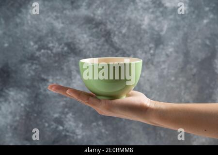 Female hand holding a green bowl on a gray background Stock Photo