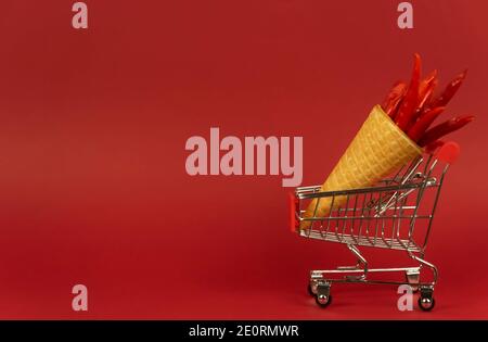 A waffle cone full of red hot chili peppers lies in a shopping trolley on a red background Stock Photo