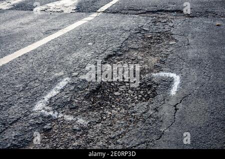 A pothole in a road in Reading, UK is marked for repair with white painted markings. However only part of the pothole is marked for repair. Stock Photo