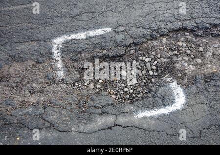 A pothole in a road in Reading, UK is marked for repair with white painted markings. However only part of the pothole is marked for repair. Stock Photo