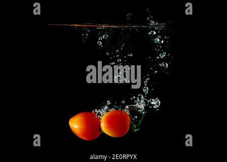 two orange fresh tomato falling into water with bubbles Stock Photo