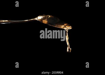clear water drips like honey over a spoon with black background Stock Photo