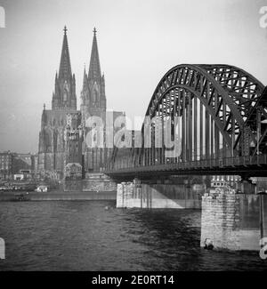 1950, historical, a post-war view from across the river Rhine of the Hohenzollern Bridge - at this time only a rail and pedestrian bridge - and the two-spired Catholic Koln Cathedral that survived the Allied bombings of WW2. Construction of this famous German landmark started in 1248 but the Gothic style church was not finally completed until much later in 1880. Stock Photo