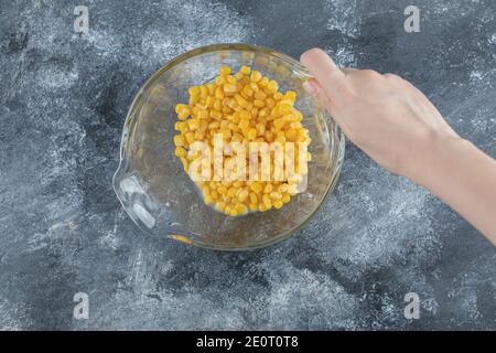 Female hand holding bowl of corns on marble background Stock Photo