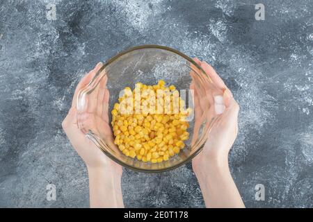 Female hands holding bowl of canned corns on marble background Stock Photo