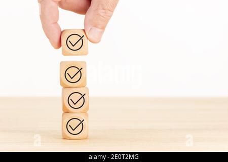 Checking or checklist concept. Hand picked wooden cube block with check icon stacked on wooden table. Copy space Stock Photo