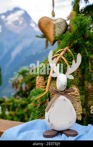 Green Christmas tree with cones growing in French Alps mountains decorated with hanging wooden heart  and christmas moose and mountain peaks on backgr Stock Photo