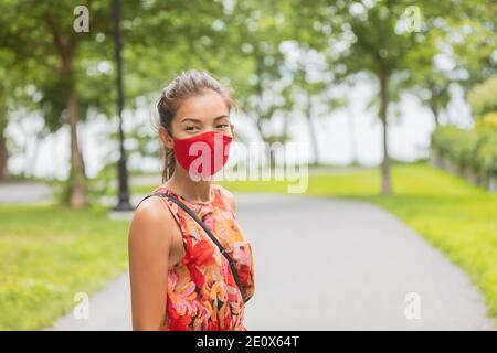 Asian woman wearing facial covering walking on street while waiting outside bus stop for public transport. Summer fashion portrait in red mask Stock Photo