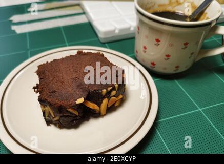 Sliced brownie cakes and hot coffee on a cutting mat at desk. Stock Photo