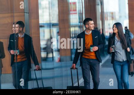 Business couple ( colleagues ) walking along the futuristic modern station (airport) while drinking coffee and talking to each other. Stock Photo