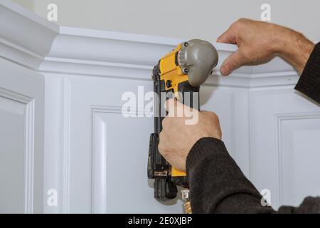 A worker using portable air gun nail in the nailing to crown moldings on new kitchen Stock Photo